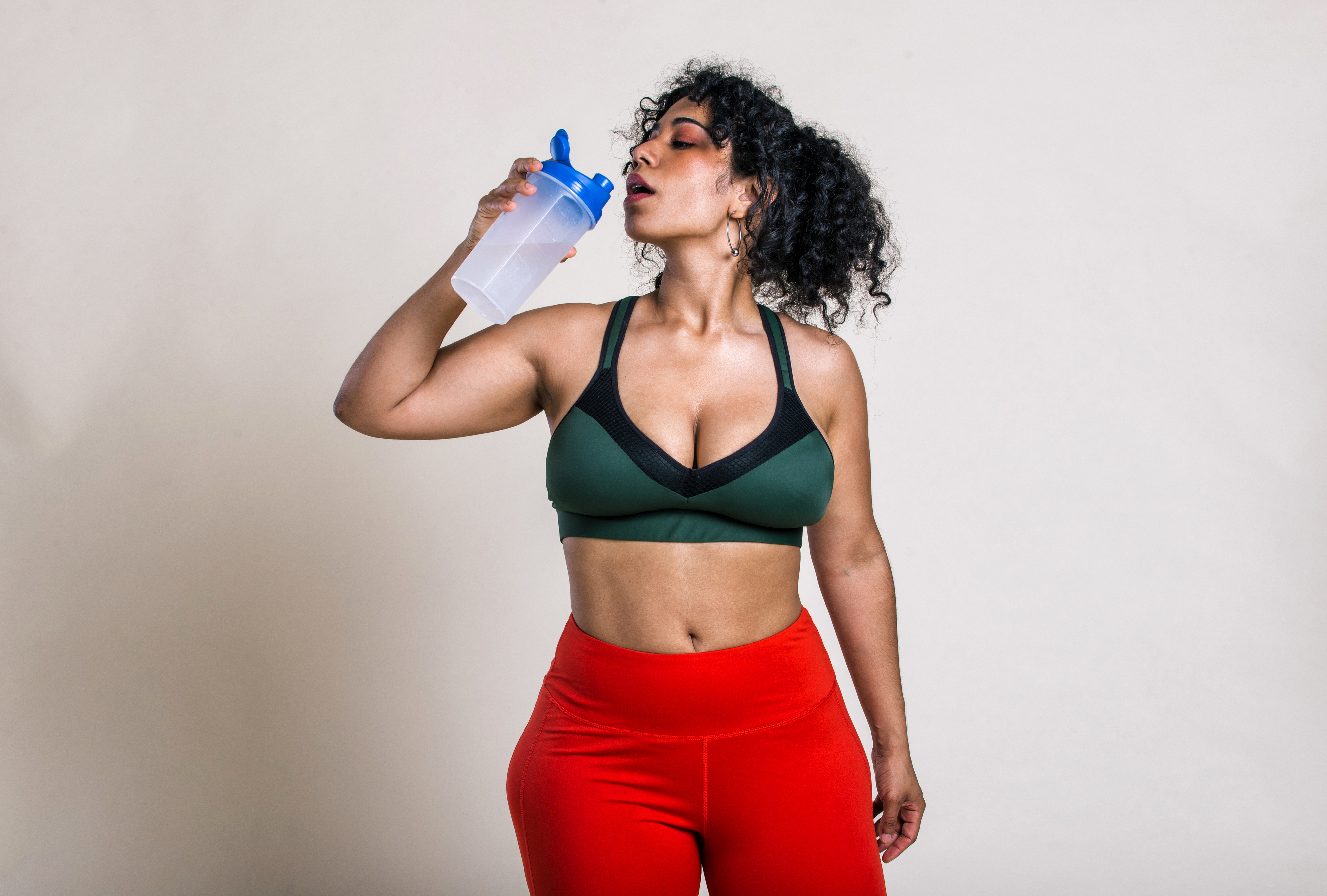 A person in workout attire drinks from a water bottle. They are wearing a sports bra and exercise leggings