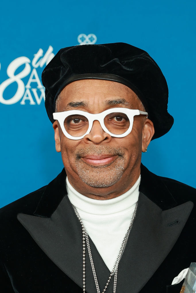 Spike Lee at an event, wearing a black beret, white round glasses, a black blazer, and a white turtleneck