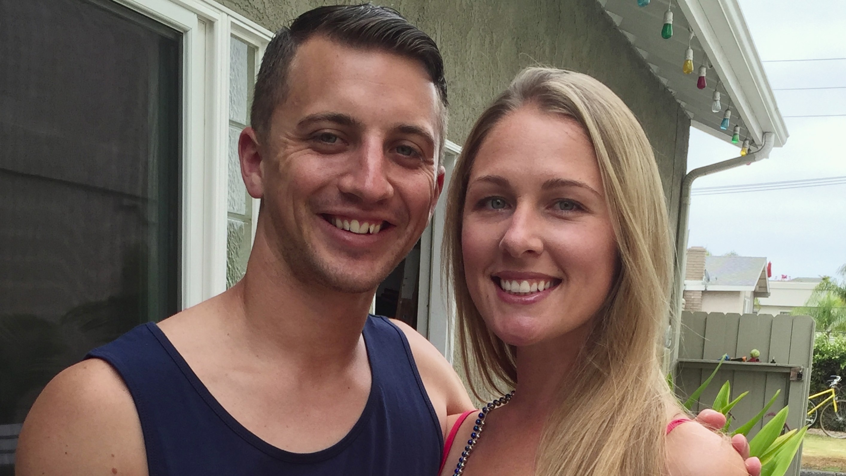 I don't know who the people in the image are. A man and a woman smile at the camera standing close together outside a house