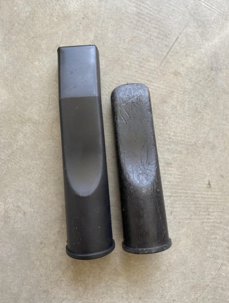 Two vacuum cleaner hose attachments lying side by side on a concrete surface. One attachment shows significant wear and tear, while the other appears newer
