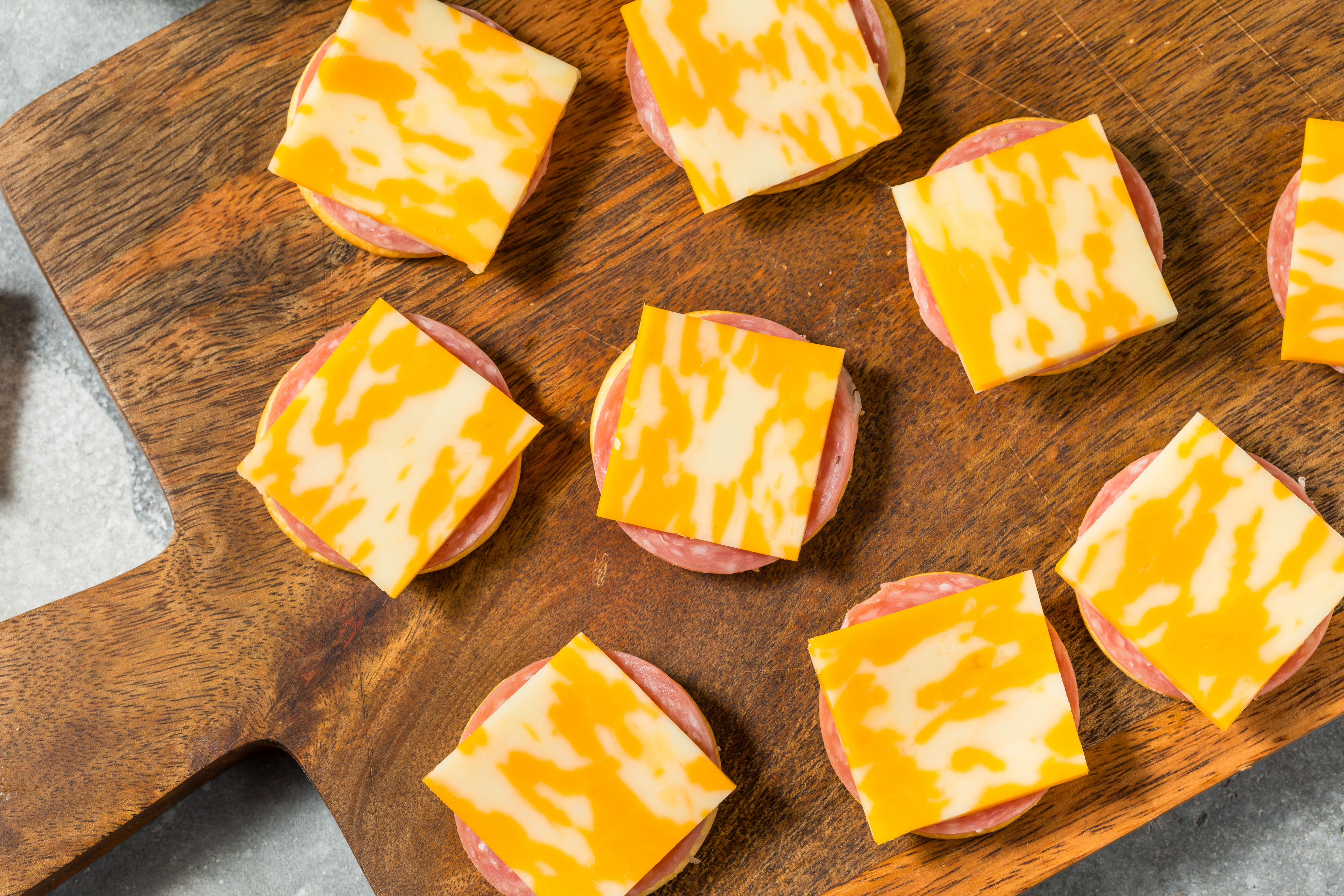 Sliced salami topped with square pieces of marble cheese arranged on a wooden cutting board