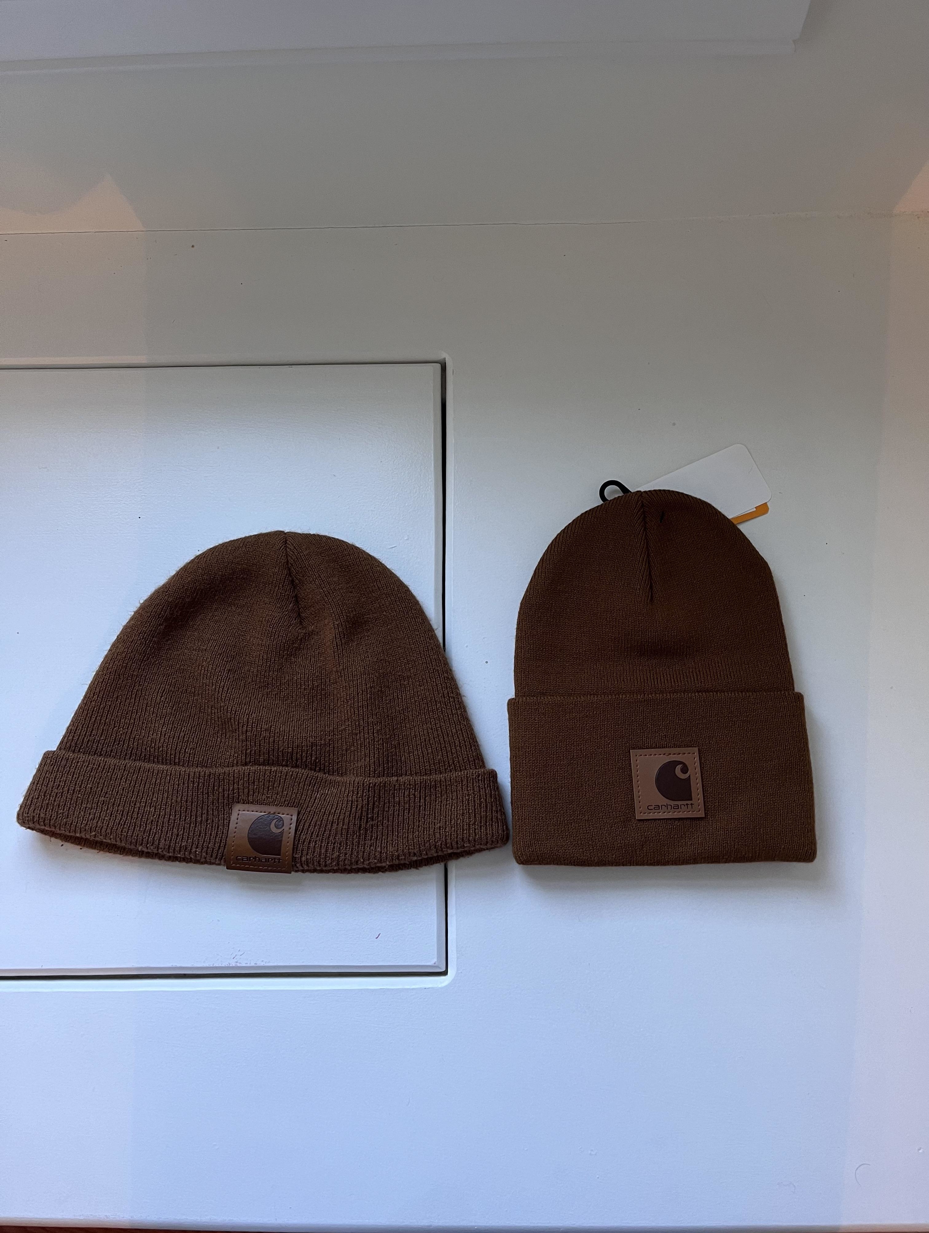 Two brown knit beanies with Carhartt brand labels are placed side by side on a white surface