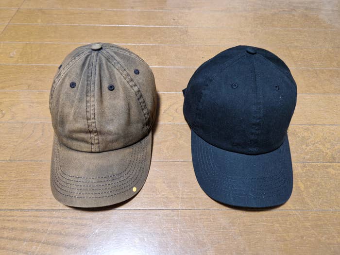 Two baseball caps placed side by side: one brown and worn, and one black and new, on a wooden surface