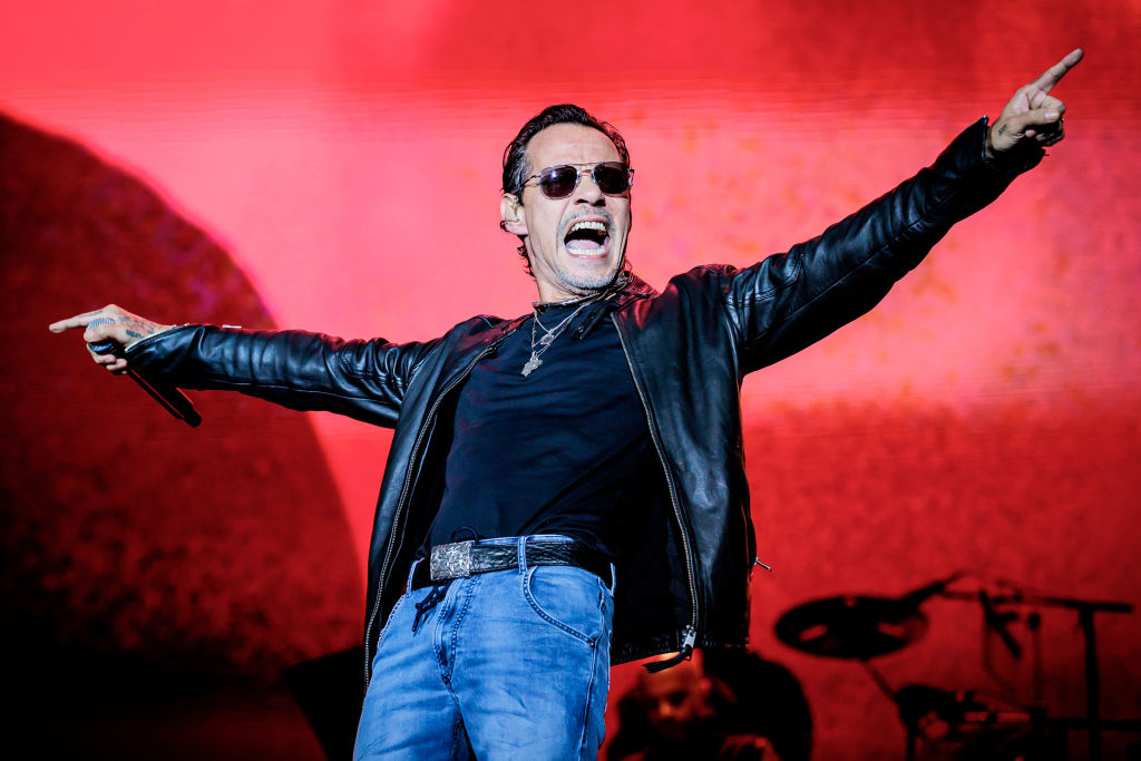 Marc Anthony performs energetically on stage, wearing a leather jacket, dark sunglasses, and jeans