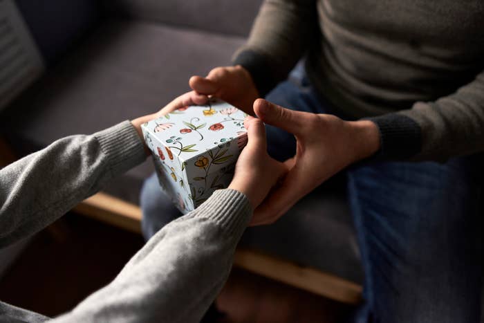 A person in a sweater gives a child a gift wrapped in flower-patterned paper