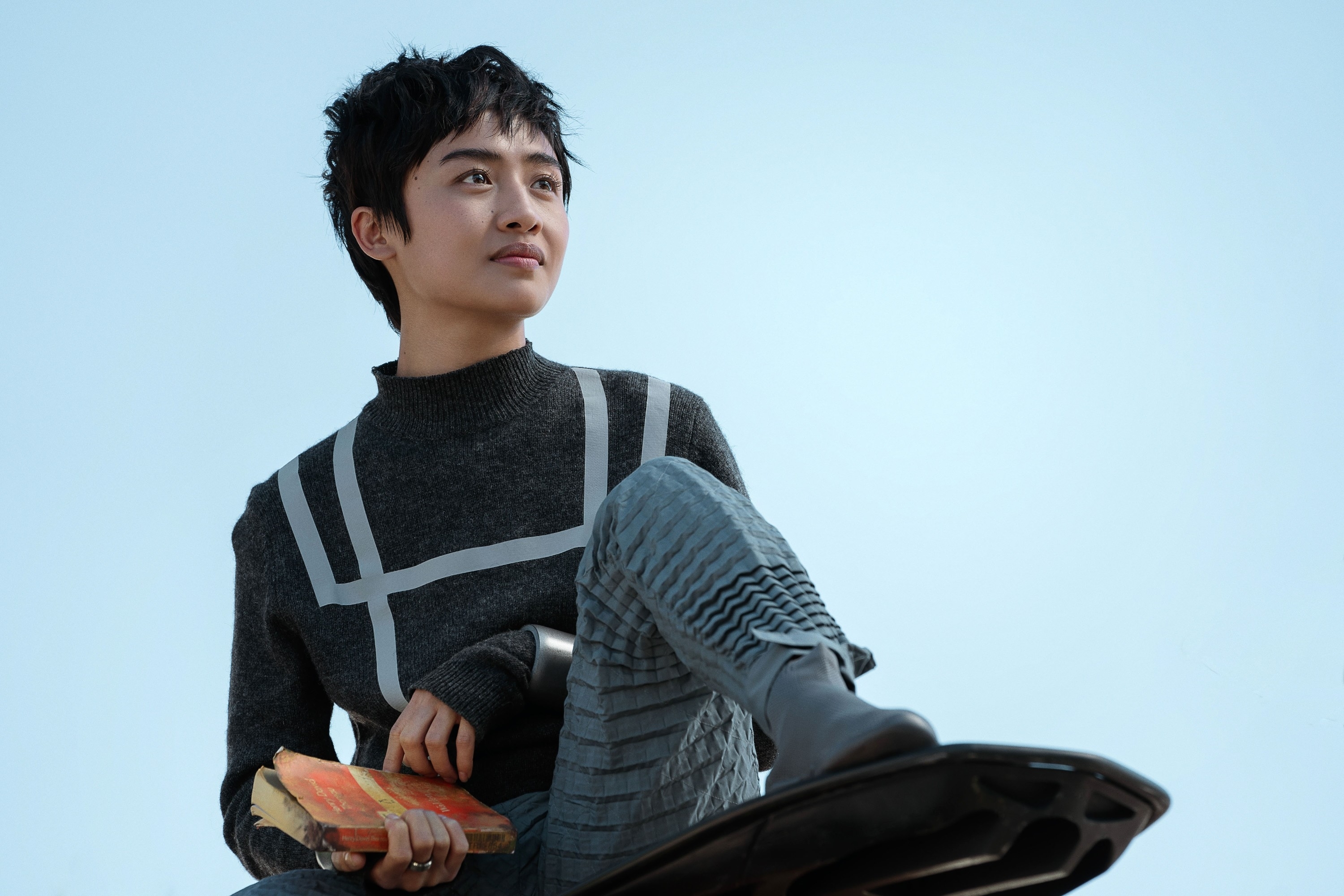 Brianne Tju wearing a futuristic suit, holding a book, and sitting on a hover board in "Uglies"