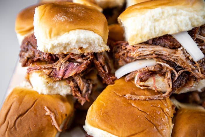 Close-up of several pulled pork sliders on soft buns, garnished with onions