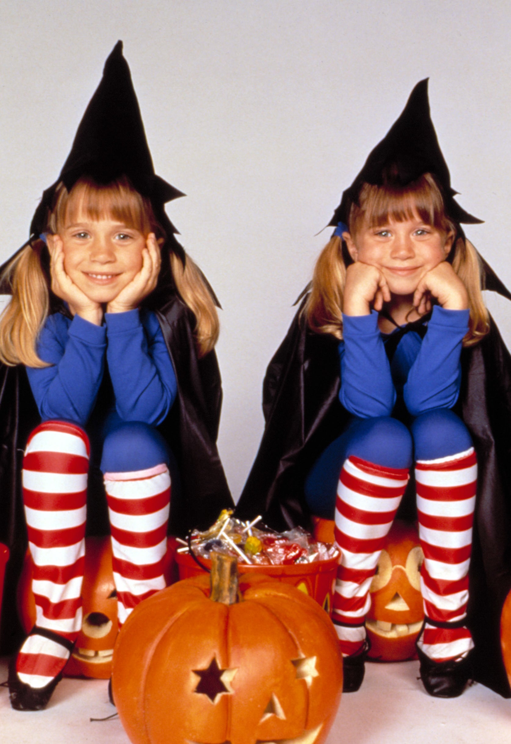 Mary-Kate and Ashley Olsen are dressed as witches with striped leggings, seated next to carved pumpkins in "Double, Double, Toil and Trouble"