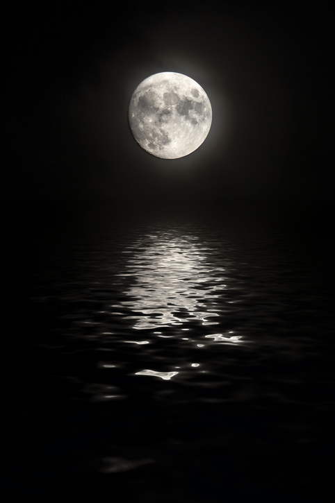 A full moon is reflected on the surface of a calm body of water during the night