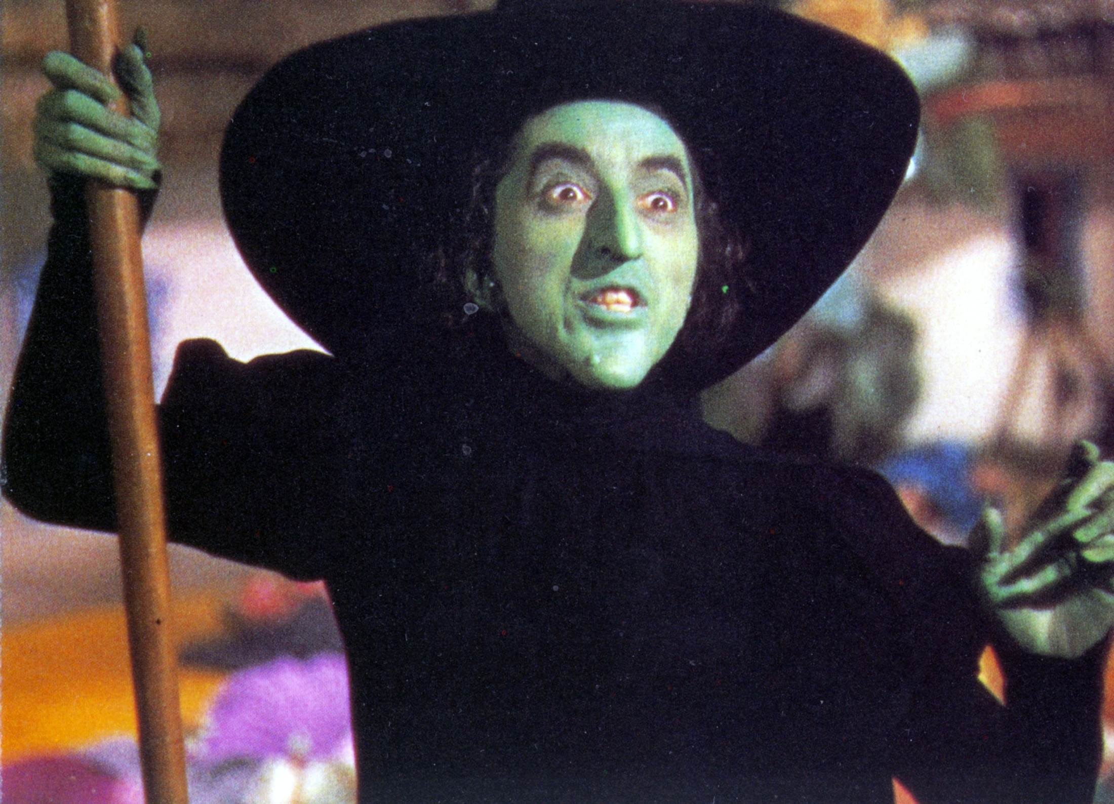 The Wicked Witch of the West holding a broom while wearing a black outfit and witch hat in "The Wizard of Oz"
