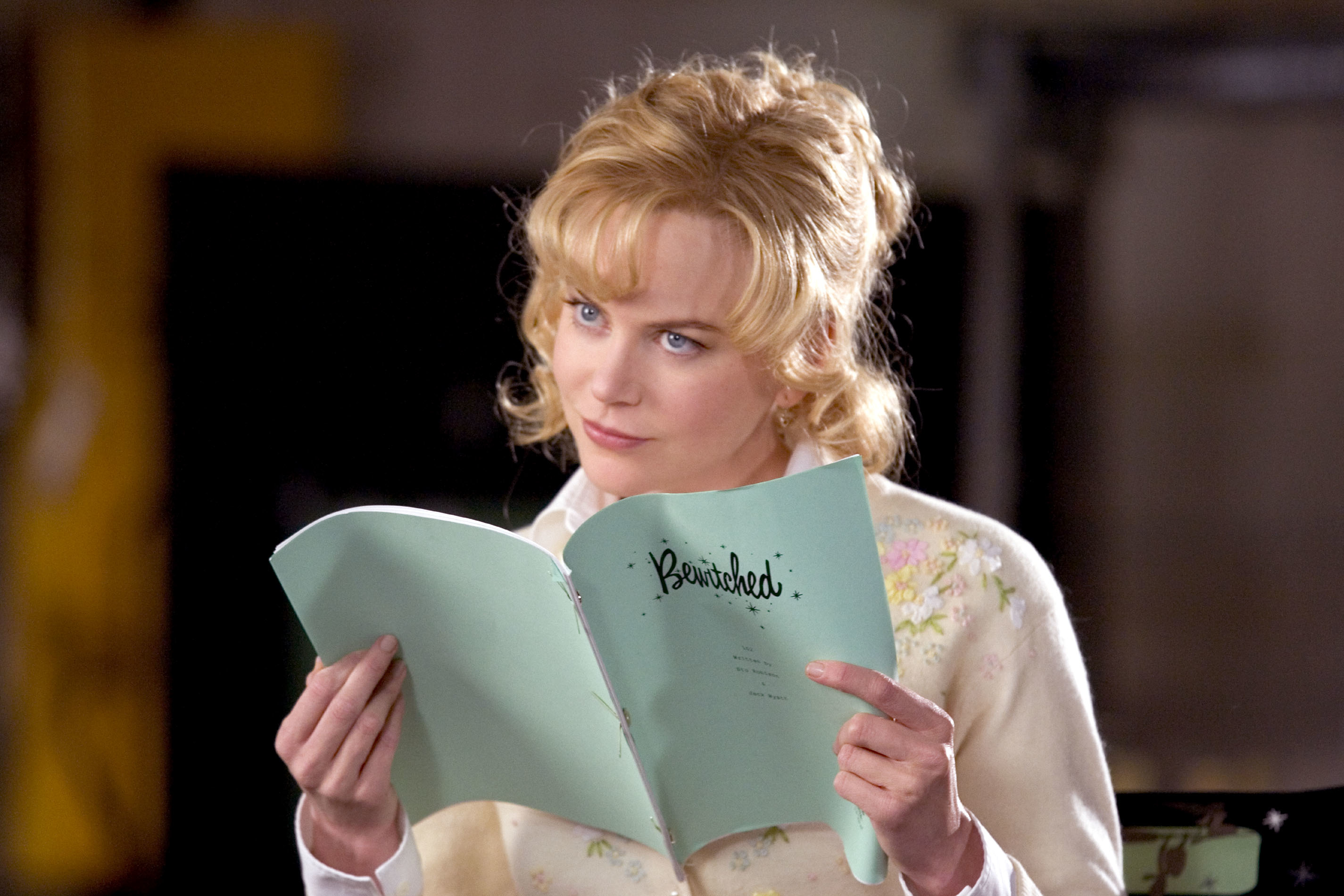 Nicole Kidman is reading a "Bewitched" script while dressed in a vintage-style outfit with a floral print sweater