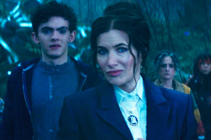 Joe Locke, Kathryn Hahn, and others in a forest scene from "Agatha All Along," with Kathryn dressed in a formal outfit and Joe in casual attire