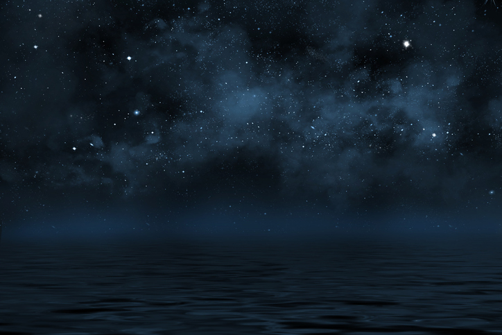 A tranquil night sky filled with stars over a calm, dark sea