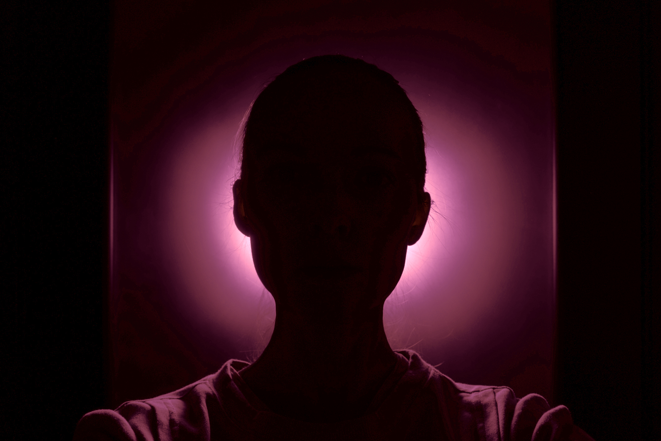 Silhouette of a person with a bright halo effect around their head from a light source in the background