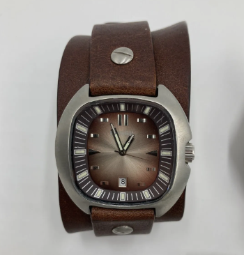 A close-up of a wristwatch with a brown leather band and a rectangular dark face, displaying the time as 10:09 and a date window showing the number 8