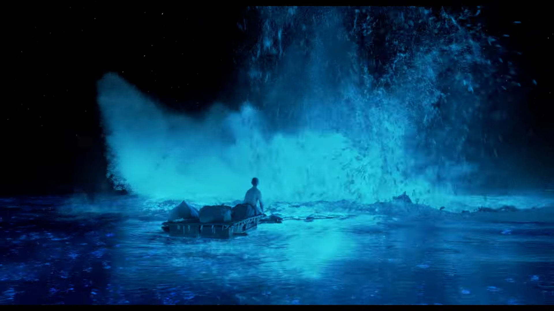 A person is sitting on a raft in an ocean at night, facing a large, luminous water splash ahead of them.