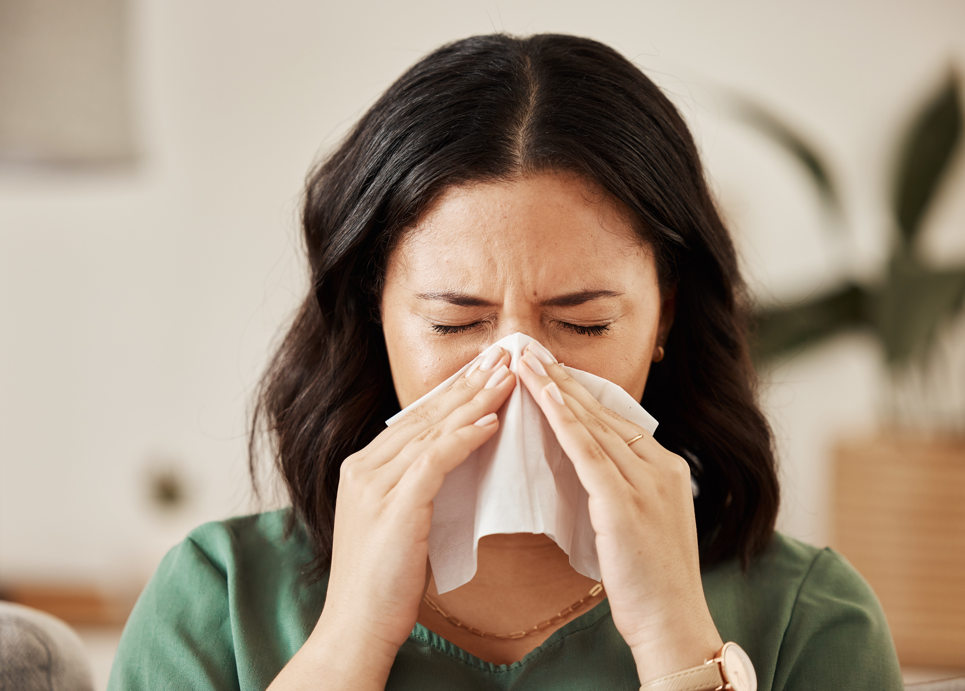 A woman sneezes into a tissue, appearing to have a cold or allergies