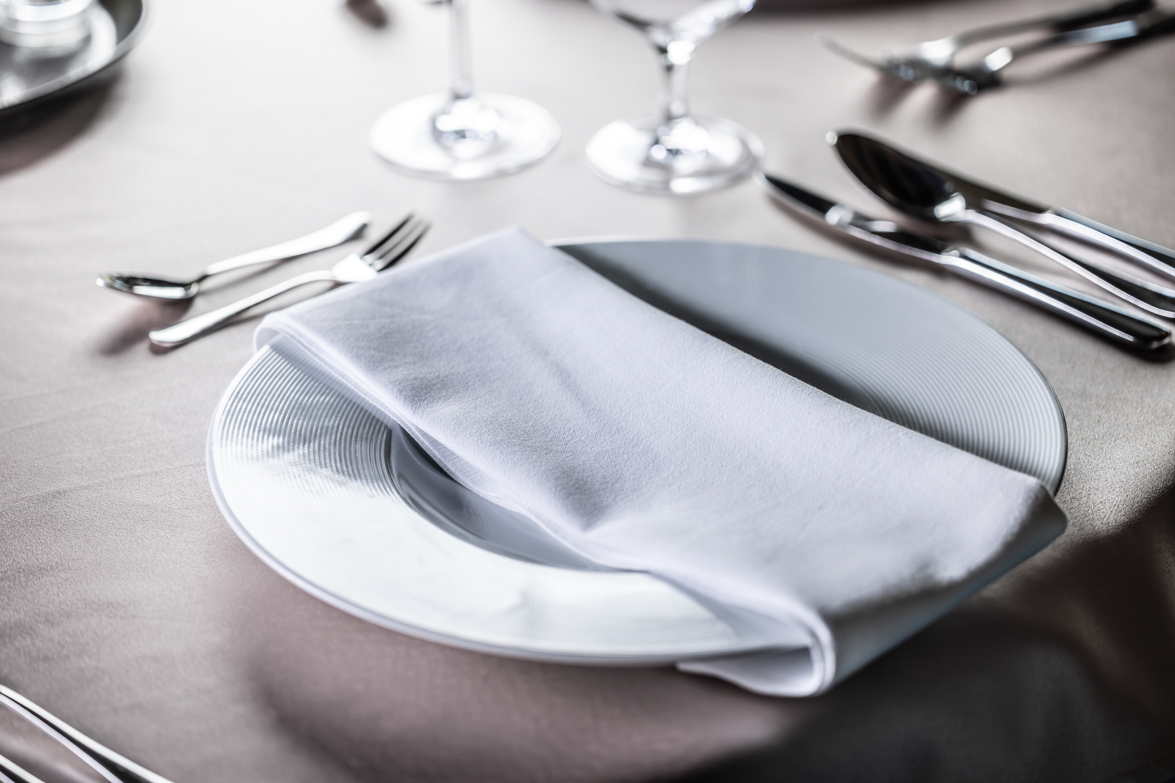 Formal table setting with a neatly folded white napkin on a plate, surrounded by cutlery and wine glasses