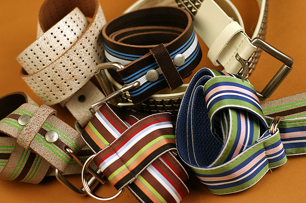 A collection of various belts made of different materials such as leather and canvas, featuring stripes and different patterns, displayed in an overlapping fashion