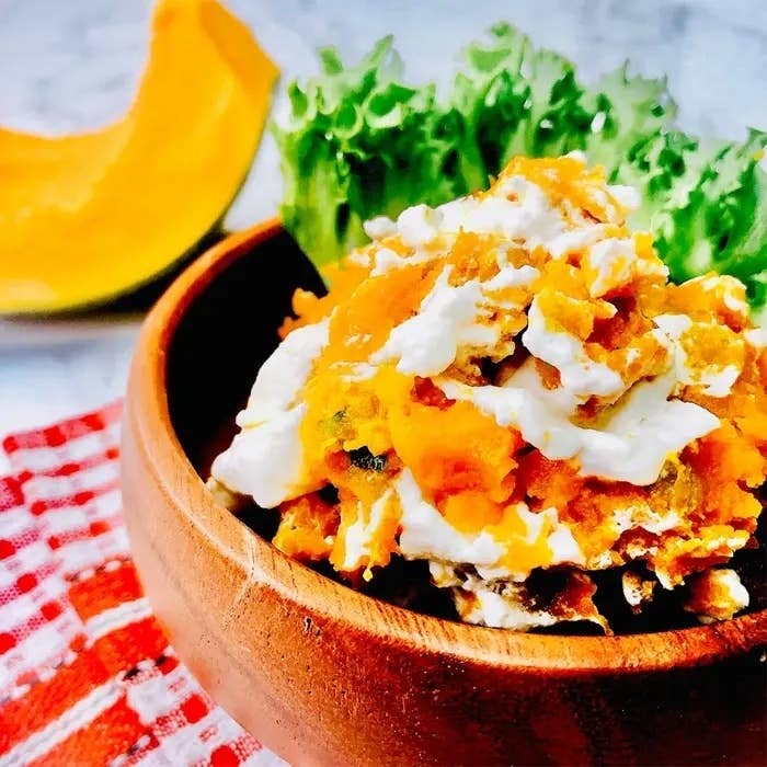 木製のボウルに盛られた料理で、かぼちゃとグリーンリーフが見えます。背景にかぼちゃのスライスも配置されています。