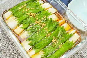 ガラスの器に並べられた野菜料理。葉っぱと白い野菜の上にゴマが振りかけられ、醤油ベースのドレッシングがかかっている。