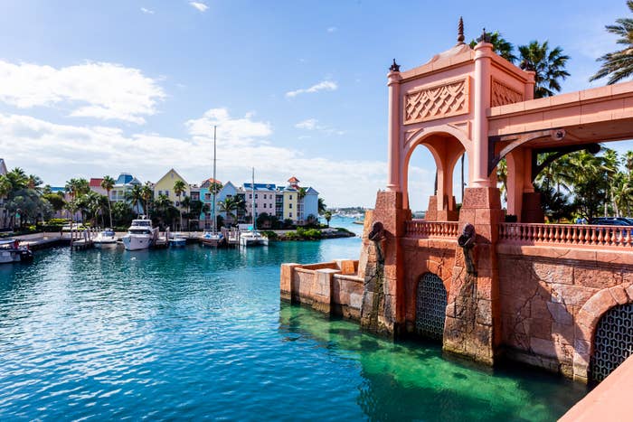 Marina in Nassau with boats docked, framed by an ornate archway and colorful buildings in the background, with palm trees and a clear sky