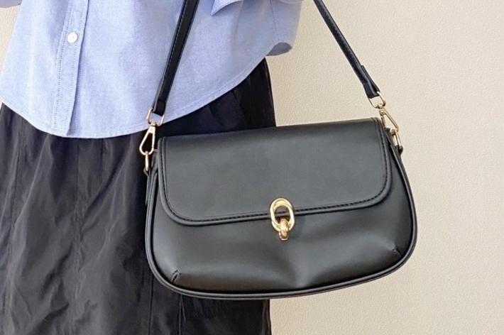 女性が黒いショルダーバッグを肩にかけている。青いシャツと黒いスカートを着ている。