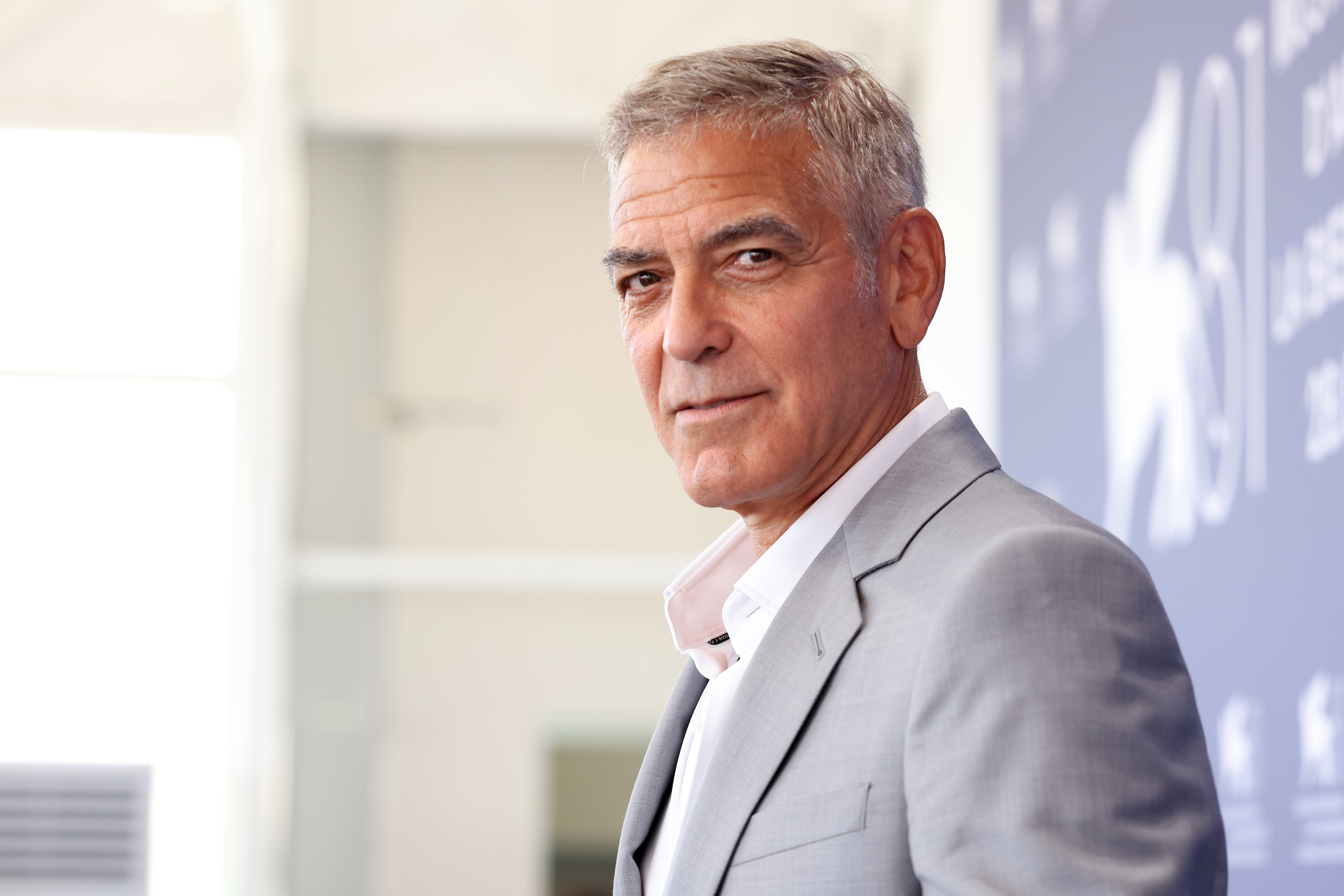 George Clooney, wearing a light suit, poses for a photo at a press event