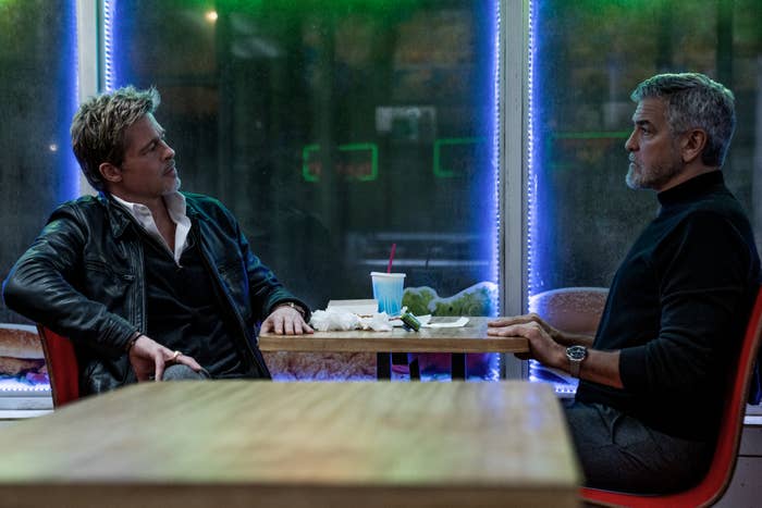 Brad Pitt and George Clooney sitting opposite each other at a table in a diner, engaged in conversation