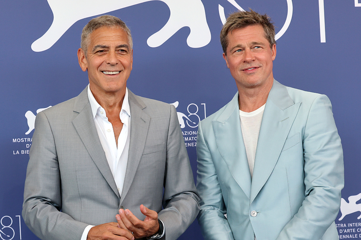 George Clooney and Brad Pitt at La Biennale di Venezia 2024, wearing stylish suits, smiling in front of a Venice Film Festival backdrop