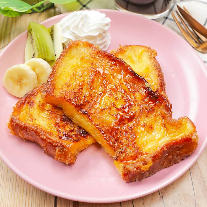 ピンクの皿に盛り付けられたフレンチトースト、ホイップクリーム、スライスされたバナナとキウイ。