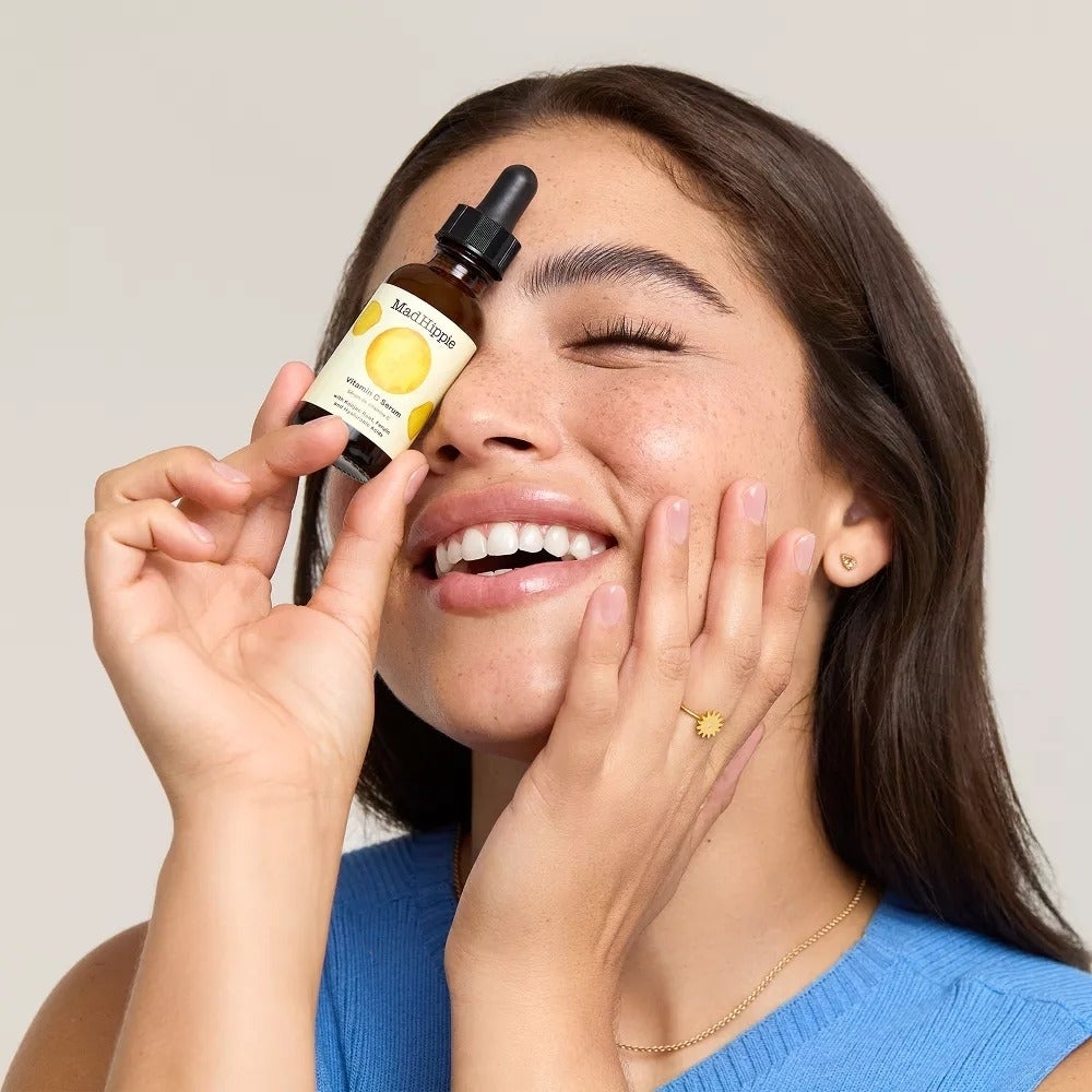 Person smiling and holding a skincare serum vessel  adjacent  to her eye, advertizing  quality   treatment