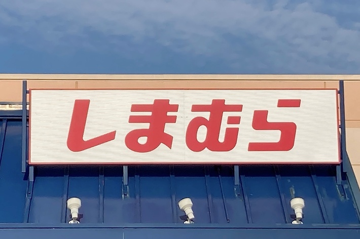 A sign with Japanese characters on top of a store entrance, reading “しまむら” (Shimamura). No individuals are in the image