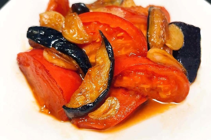 白い皿に盛り付けられたトマトとナスの炒め物。