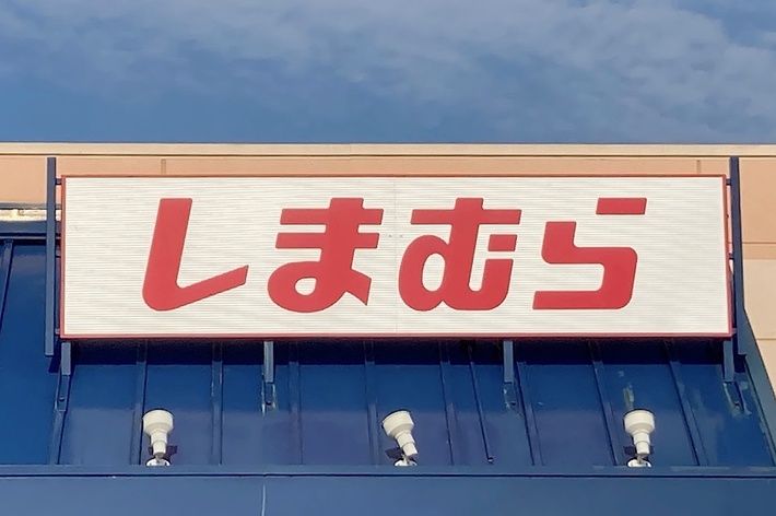 Storefront with a sign displaying Japanese text in red, located under a clear sky