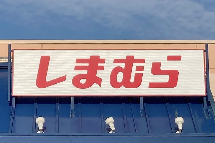 A Japanese store with the name “Shimamura” on a sign above the entrance. The store has a blue awning and accessibility parking in front