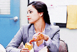 Stephanie Beatriz as Rosa Diaz from Brooklyn Nine-Nine eating a snack at a table, wearing a business suit