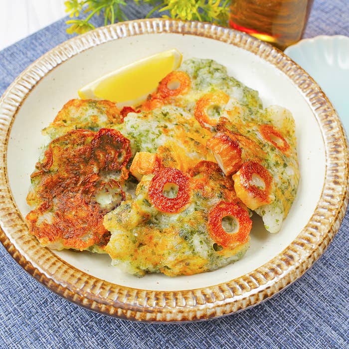 レモンのくさび片を添えた料理が皿に盛られている。背景には食卓の一部が見えている。