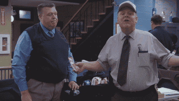 Charles Boyle and Raymond Holt from Brooklyn Nine-Nine are standing together in an office. Boyle looks indifferent, while Holt animatedly gestures with his hands