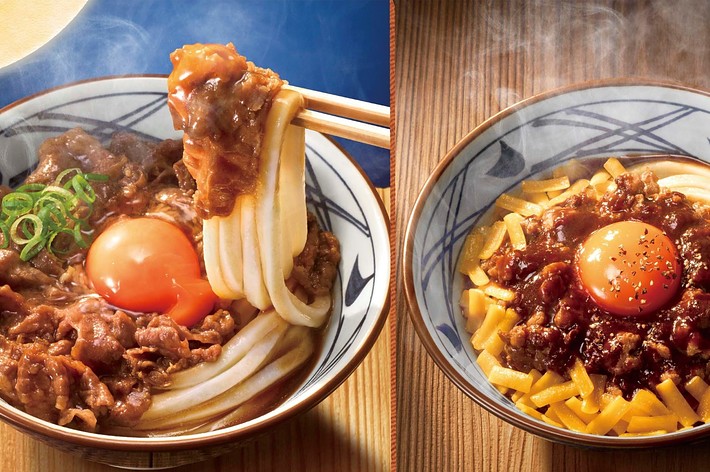 2つのうどんの写真。左は肉うどん、右は温泉卵と肉が盛られたうどん。いずれも湯気が立ち上がっている。丸亀製麺のロゴあり。