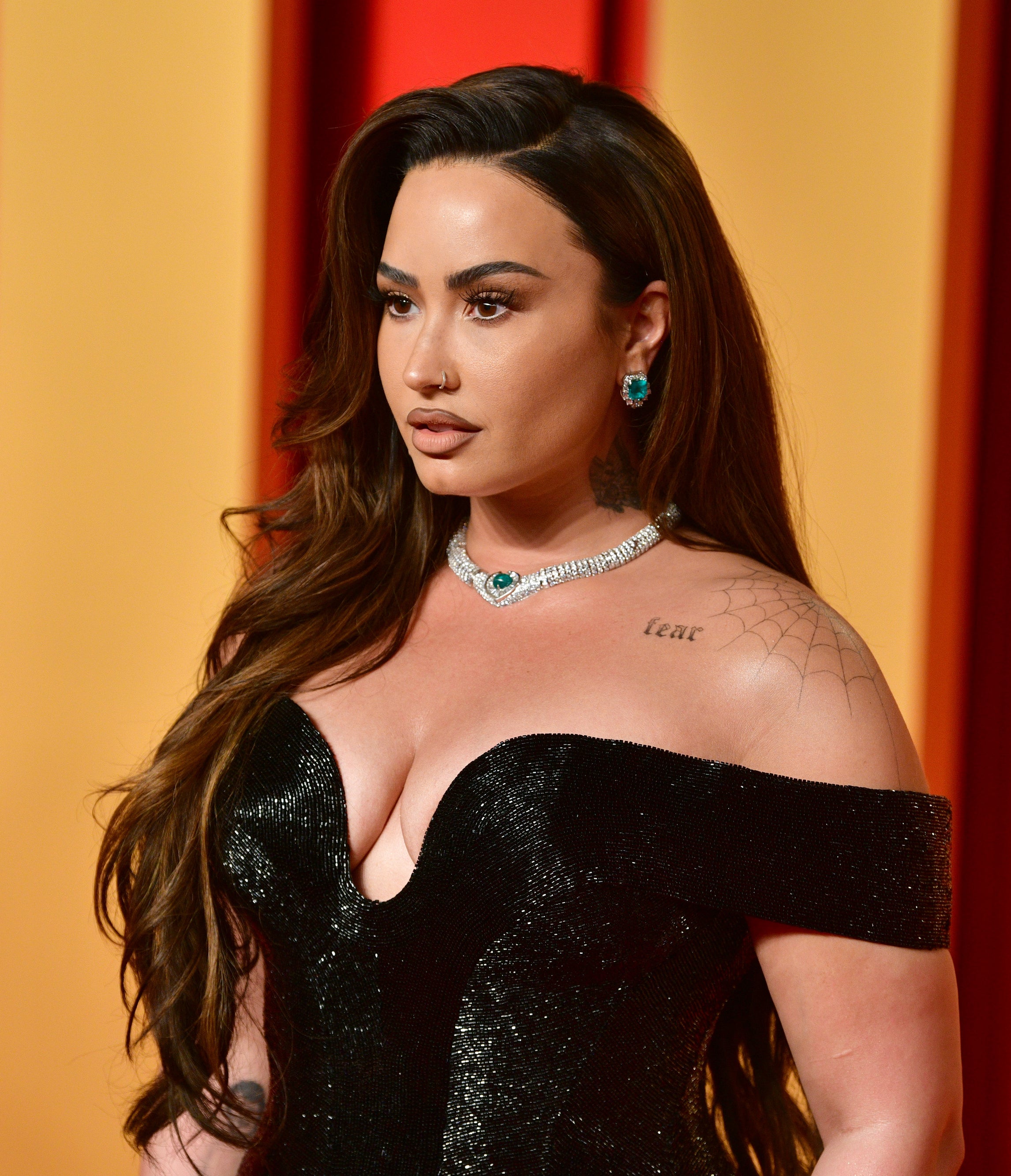 Demi Lovato stands on the red carpet, wearing an off-shoulder velvet dress, with diamond jewelry and styled hair