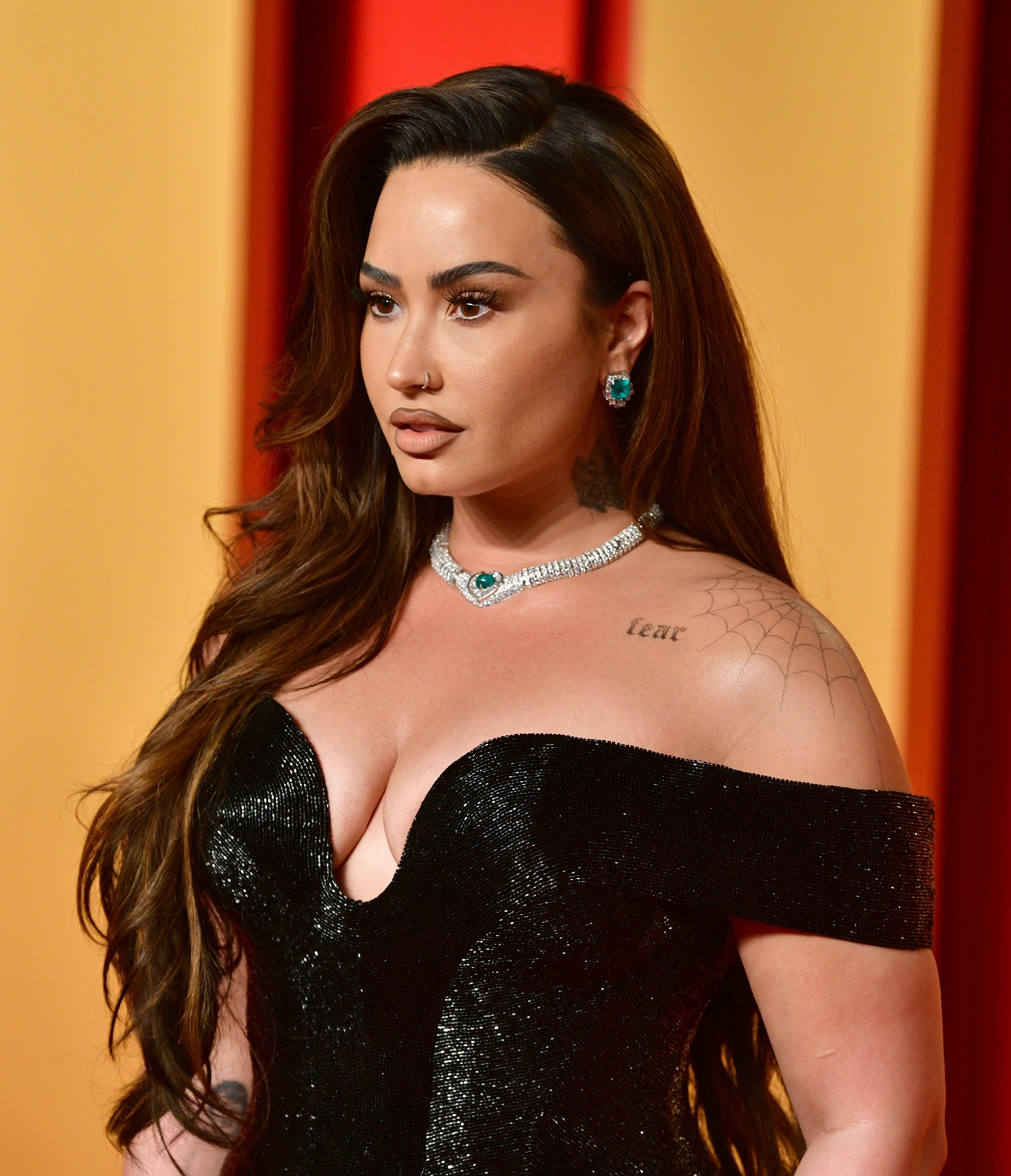 Demi Lovato stands on the red carpet, wearing an off-shoulder velvet dress, with diamond jewelry and styled hair