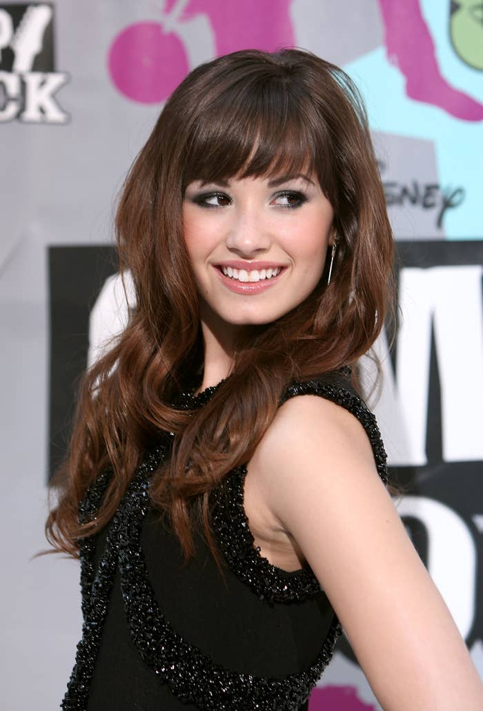 Demi Lovato is smiling at a public event, wearing a sleeveless, outfit with a textured design