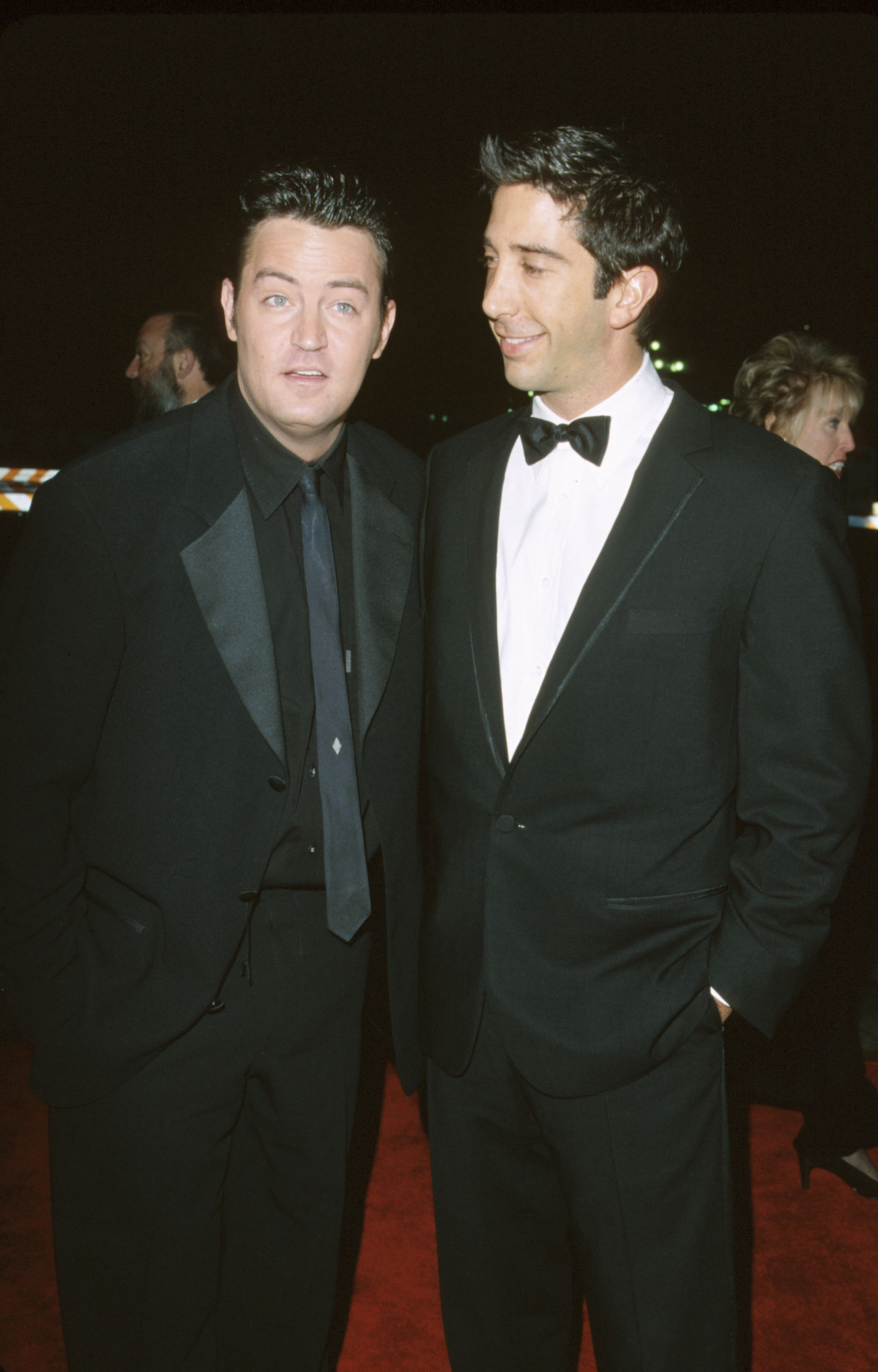 Matthew Perry and David Schwimmer on the red carpet in dark tuxedos, smiling at an event