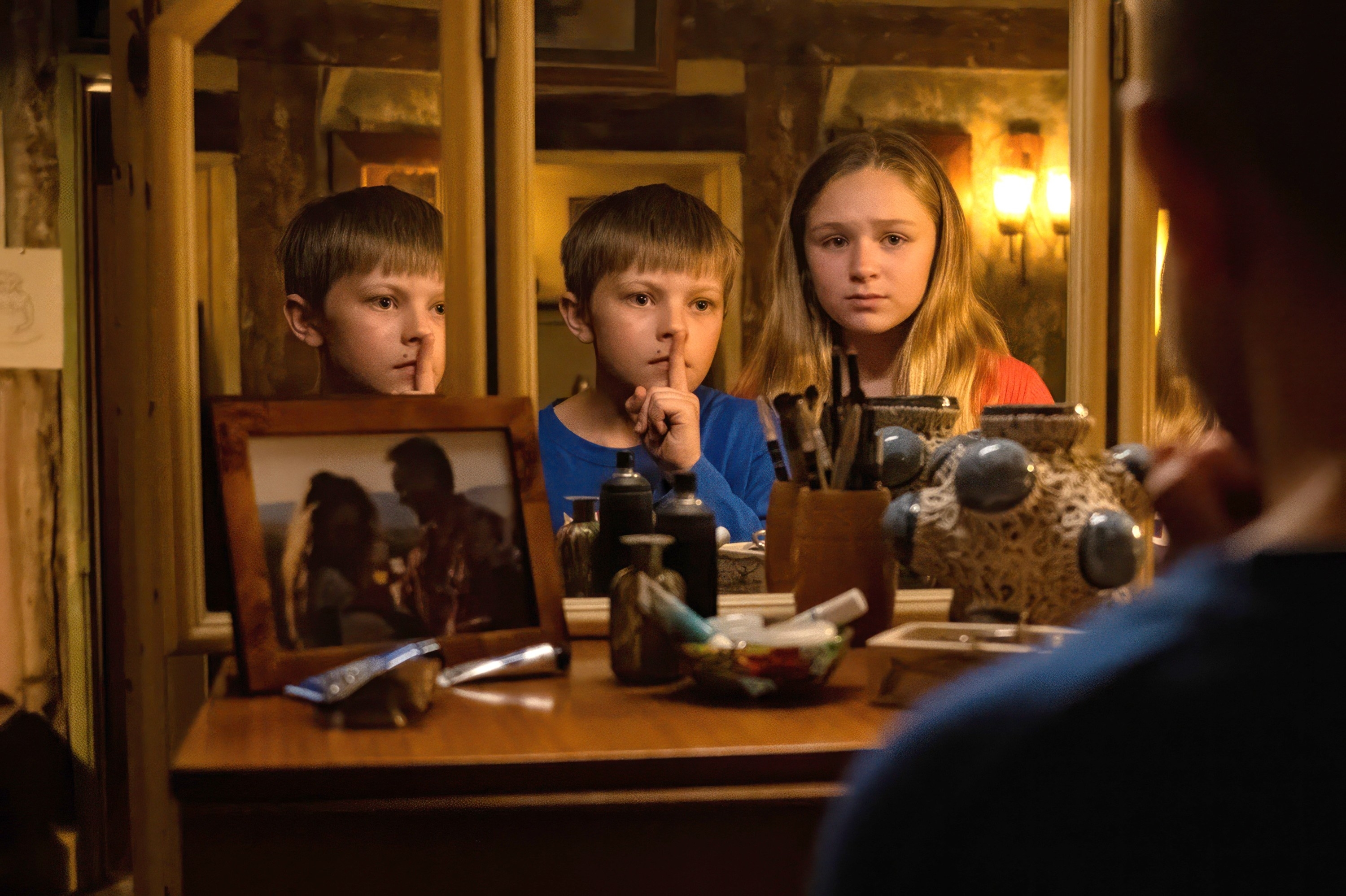 Two children, portrayed by Millicent Simmonds and Noah Jupe, are in front of a mirror with fingers over their lips, suggesting silence