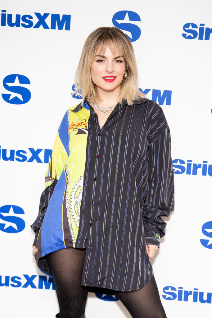JoJo on the red carpet, wearing an oversized striped shirt with mixed patterns and black tights at a SiriusXM event