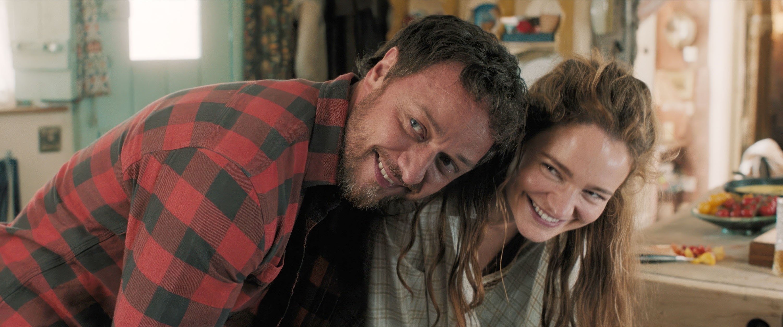 James McAvoy and Claire Foy smile as they lean together inside a cozy, rustic setting