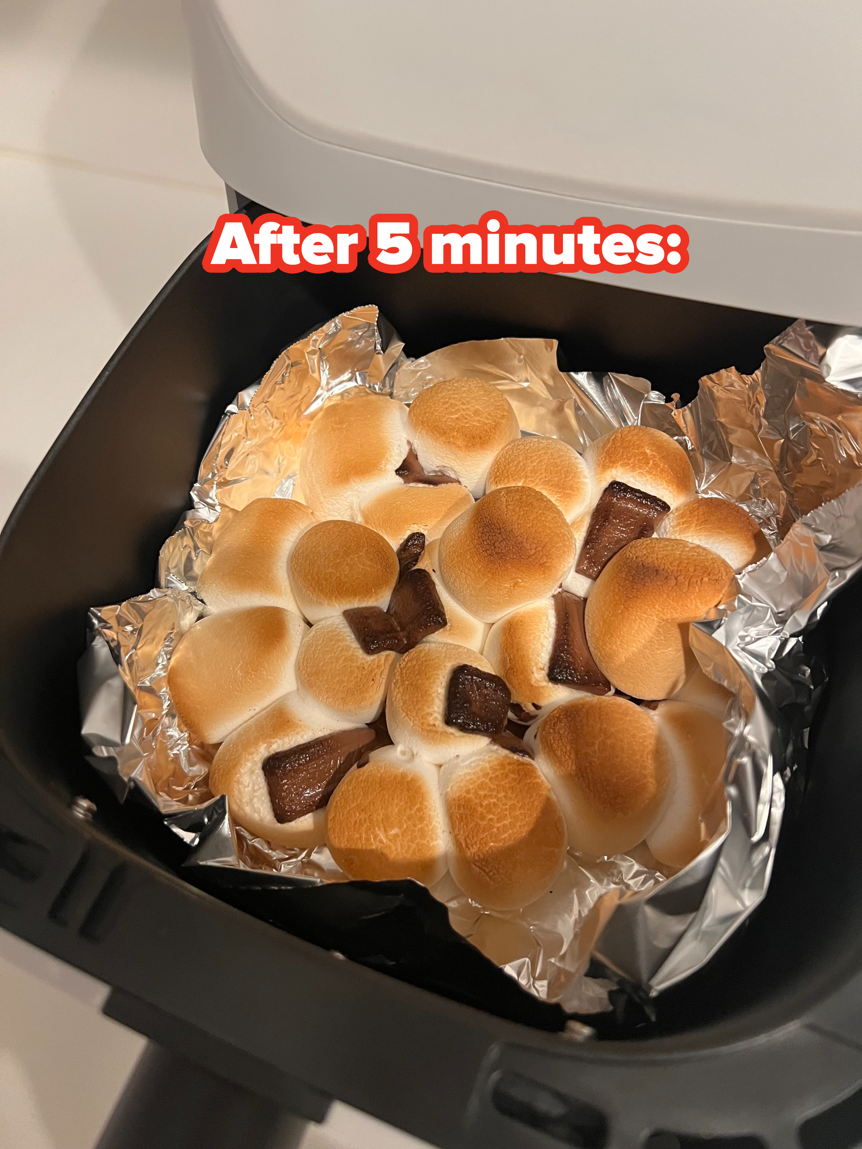 Toasted marshmallows with melted chocolate chunks on aluminum foil inside a container