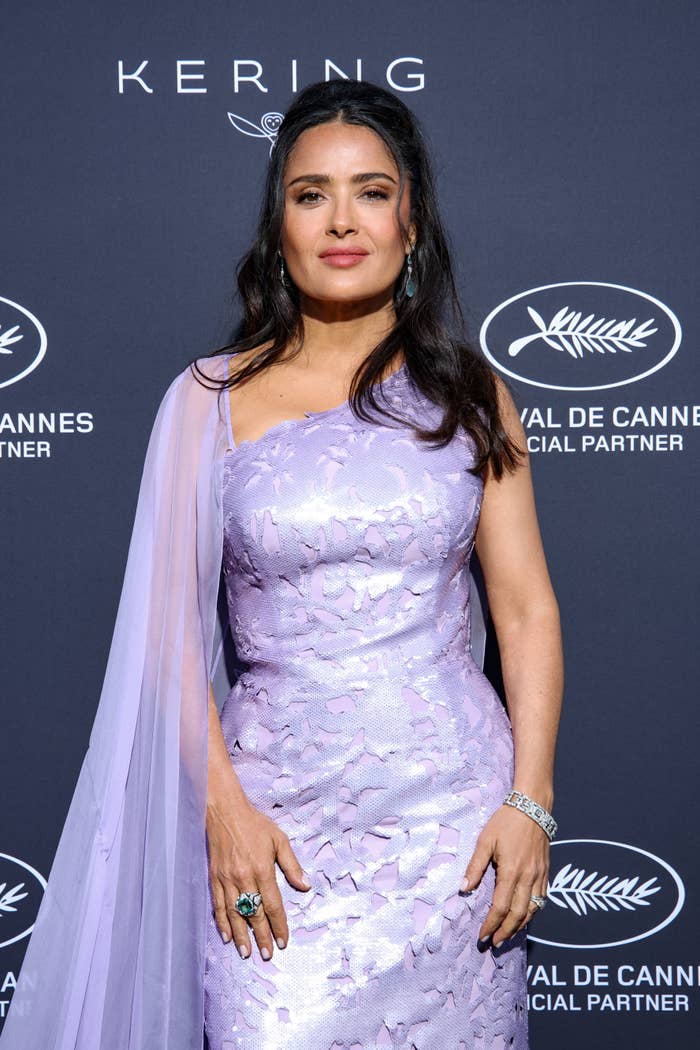 Salma Hayek on the red carpet at the Cannes Film Festival, wearing an elegant one-shoulder dress with intricate detailing and matching accessories
