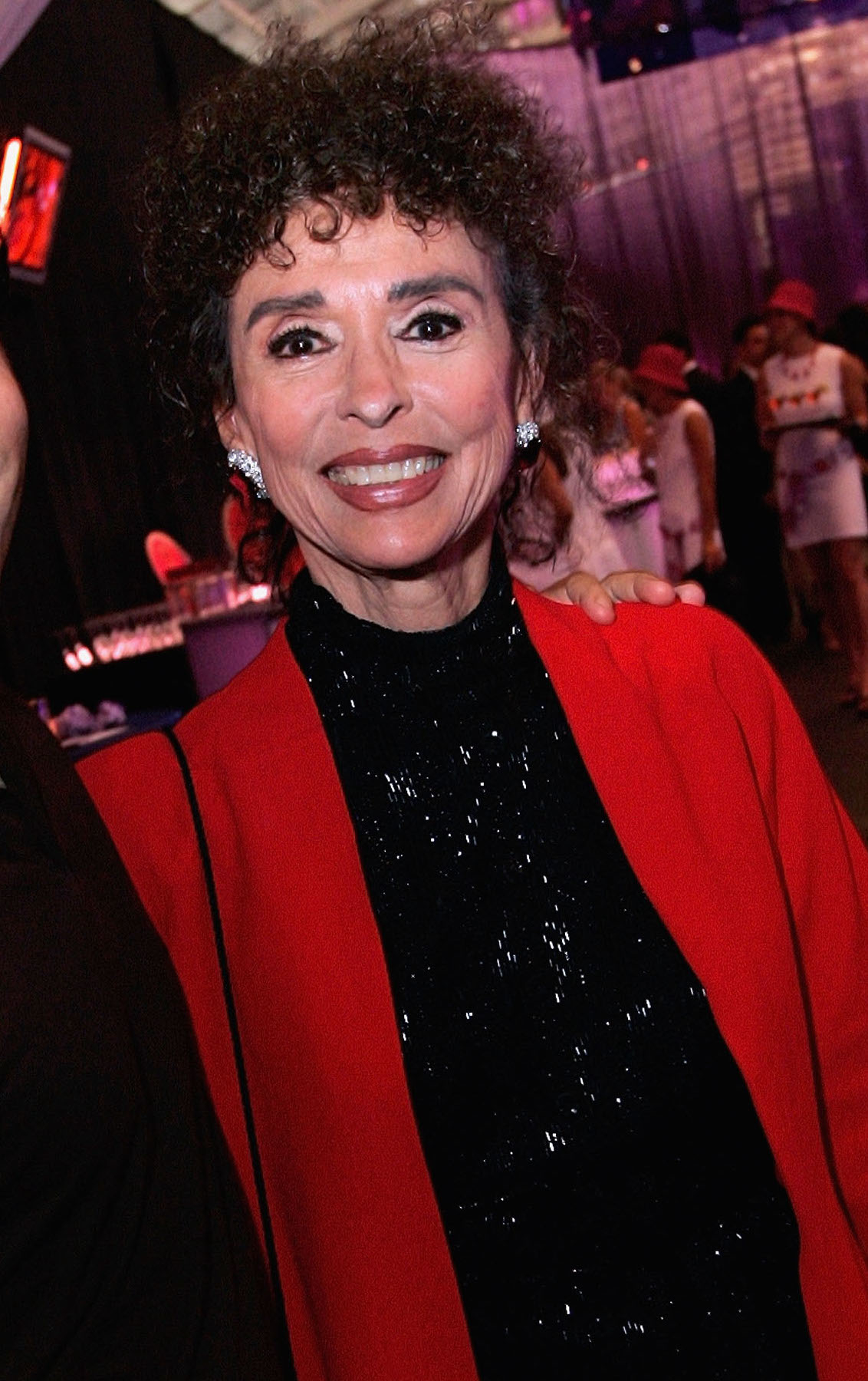 Woman in a black sparkling dress with a red shawl smiles at an event